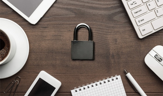 Lock on table surrounded by iPhone, iPad, laptop, coffee, paper clips, pen, notepad, and electronic mouse