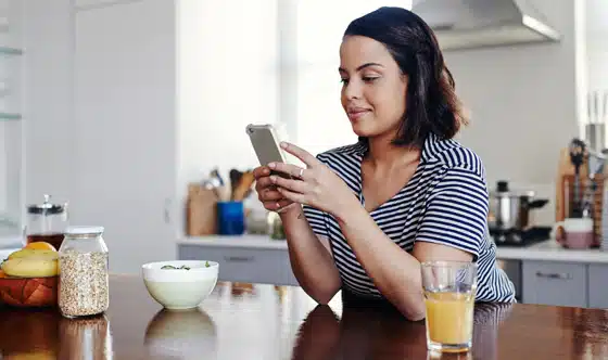 woman having breakfast in kitchen pauses to look on cell phone