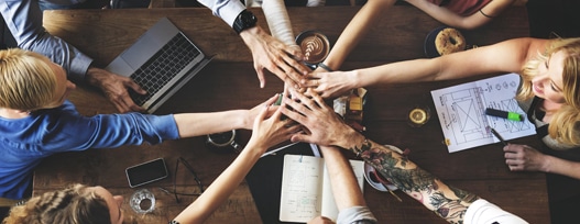 group of diverse individuals at table with hands in the middle joined together