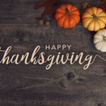 Pumpkins, leaves, and acorns on wood board background with "Happy Thanksgiving" text.
