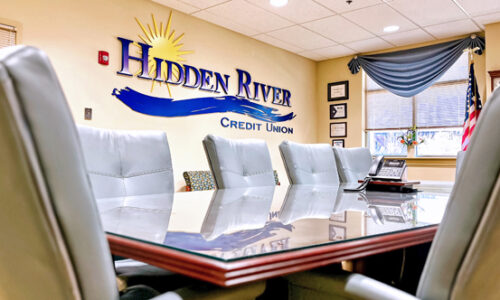 HRCU Boardroom with empty chair around conference table and blue logo on cream wall