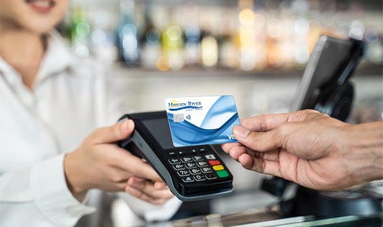 woman holding payment terminal and many holding HRCU credit card over the top of the terminal with blurred out restaurant background