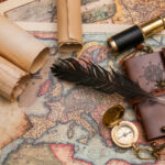 Navigation tools and a feather pen sitting on top of a map of the world.