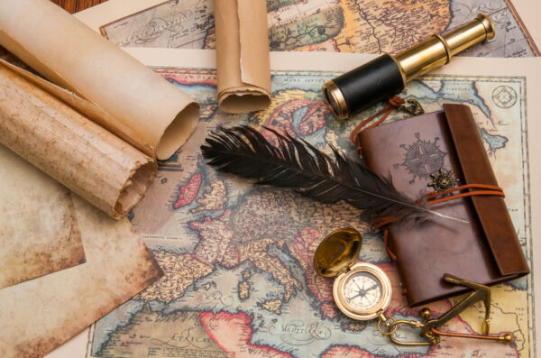Navigation tools and a feather pen sitting on top of a map of the world.
