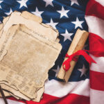 The Declaration of Independence and a wrapped scroll laying on an American flag background.