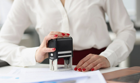 Woman sitting at a desk stamping something on a piece of paper.
