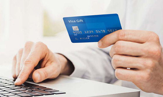 Person sitting at a laptop holding a VISA gift card and typing.