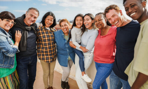 Group of multigenerational friends smiling in front of camera - Multiracial people of different ages having fun together - Main focus on center faces diverse group of people looking at the camera and smiling in casual attire and a sunny backdrop