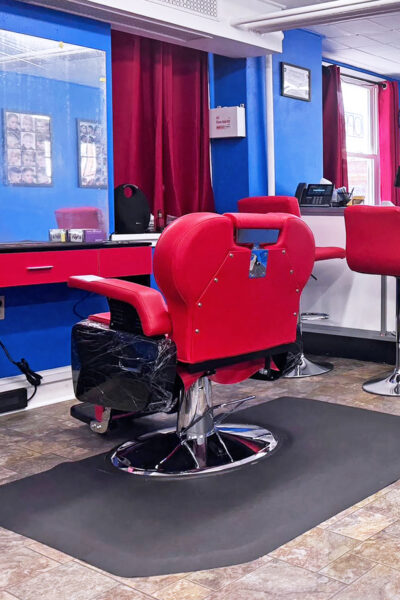 red barber's chair in front of a mirror and several red stools surrounded by royal blue walls